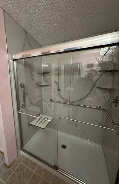 Zero-threshold walk-in shower with marble walls, grab bars, and fold-down seat
