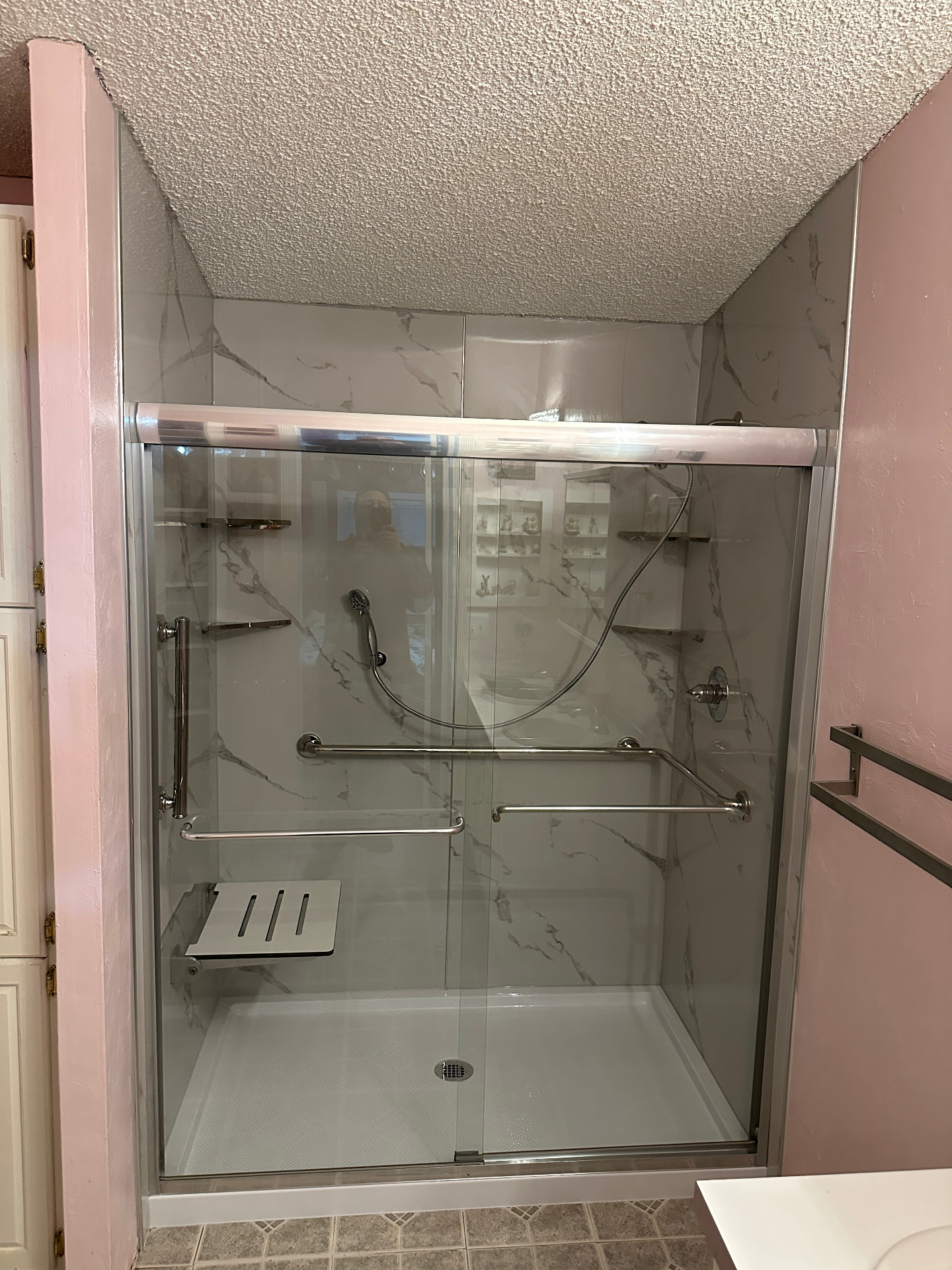 ADA compliant walk-in shower with grab bars, fold-down seat, and marble wall surround