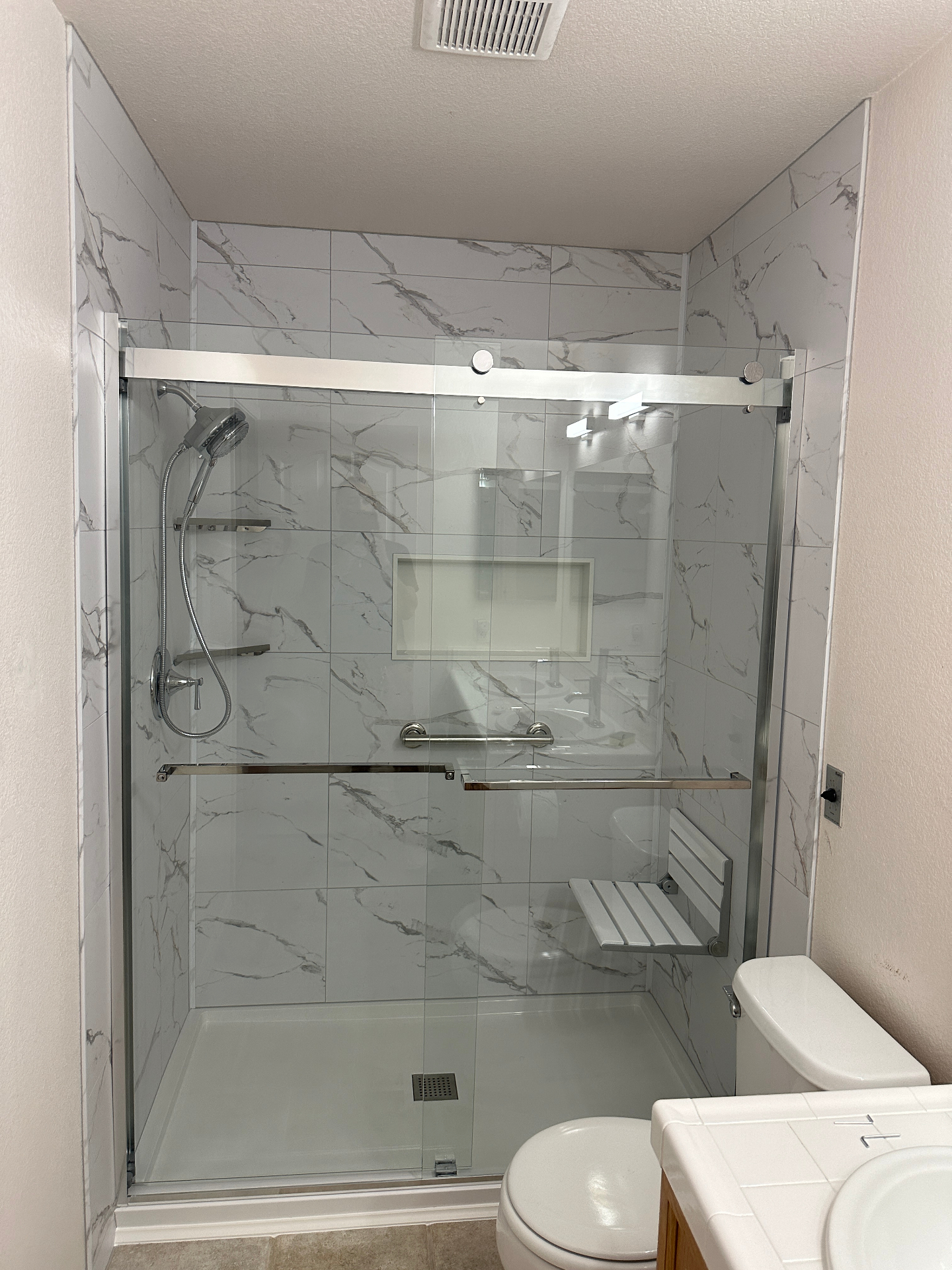 Accessible walk-in shower with marble tile, grab bars, fold-down seat, and handheld showerhead installed by Secure Bath