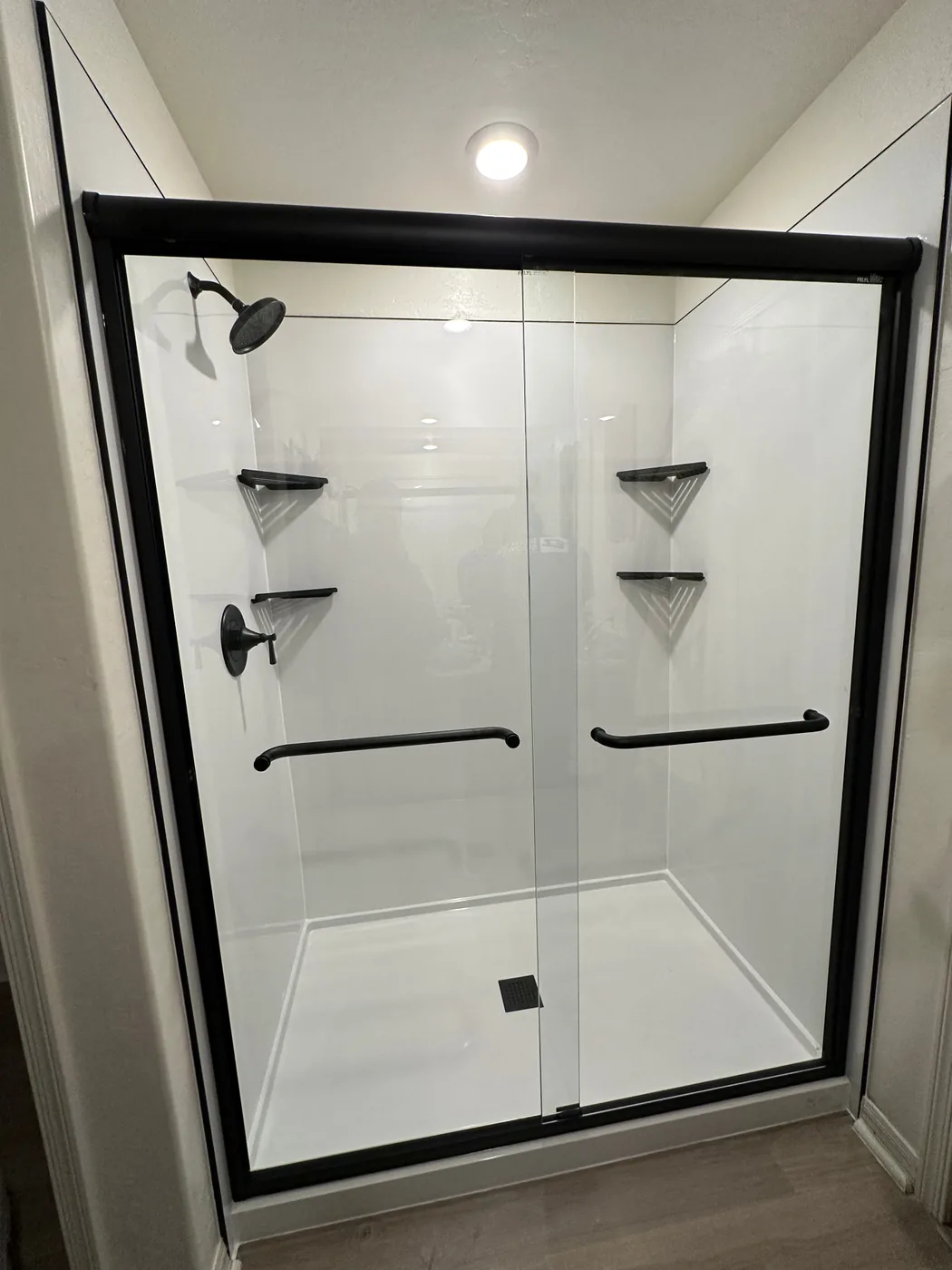 Walk-in shower with slip-resistant flooring, glass doors, and safety grab bars